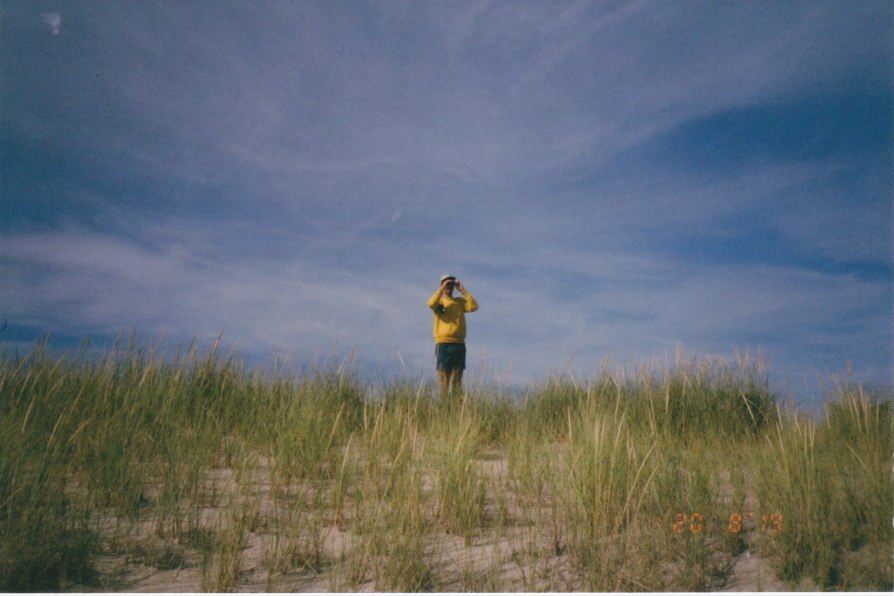 person on dunes wearing bright yellow shirt looks through binoculars