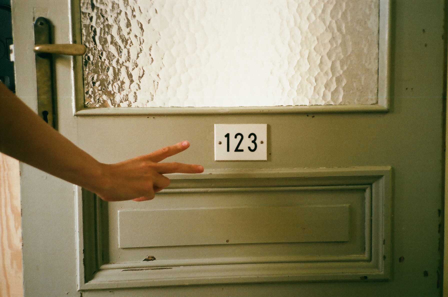 person's hand holding a peace sign under a sign on door that reads 123