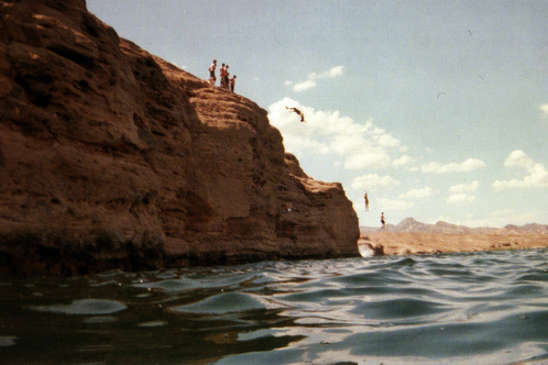 view from lake of people recreationally jumping off of cliffs