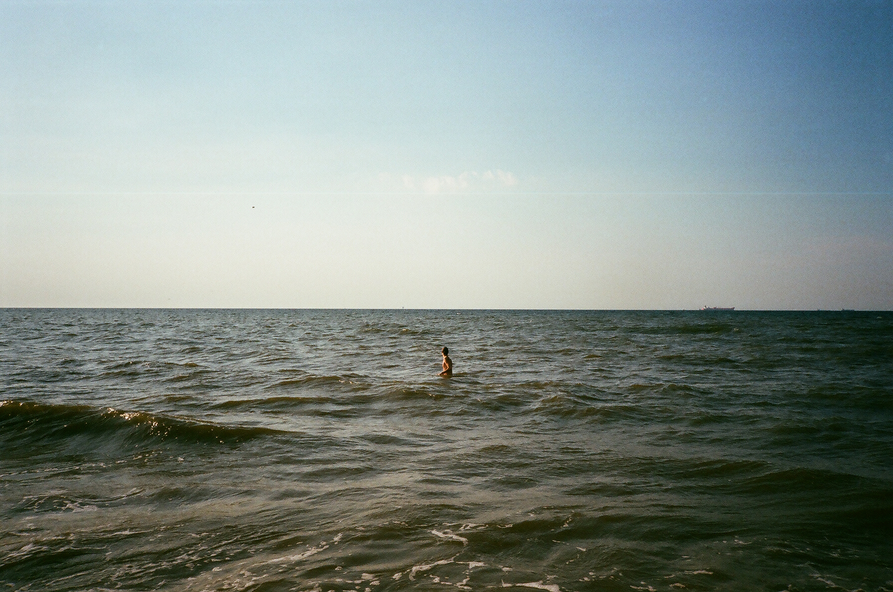 person stands in shallow sea and turns toward horizon