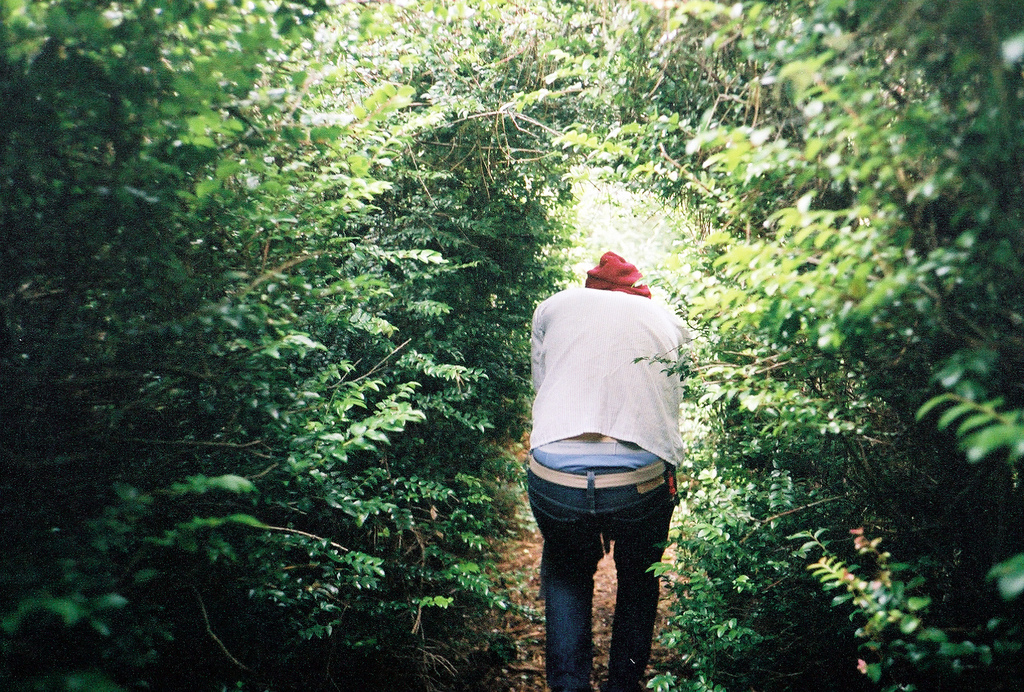 person crouching through a tunnel of bushes