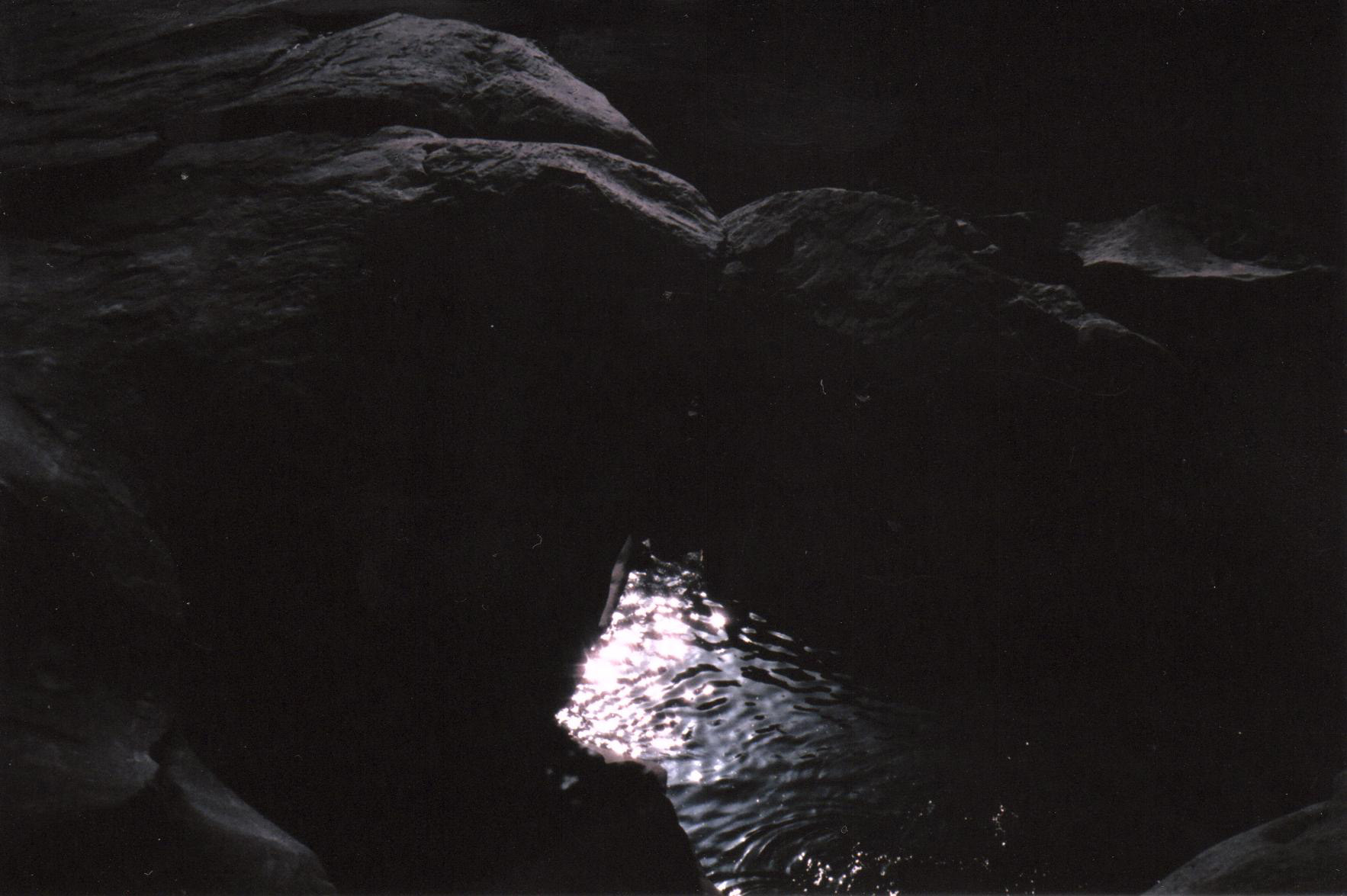sun reflecting on water between rocks
