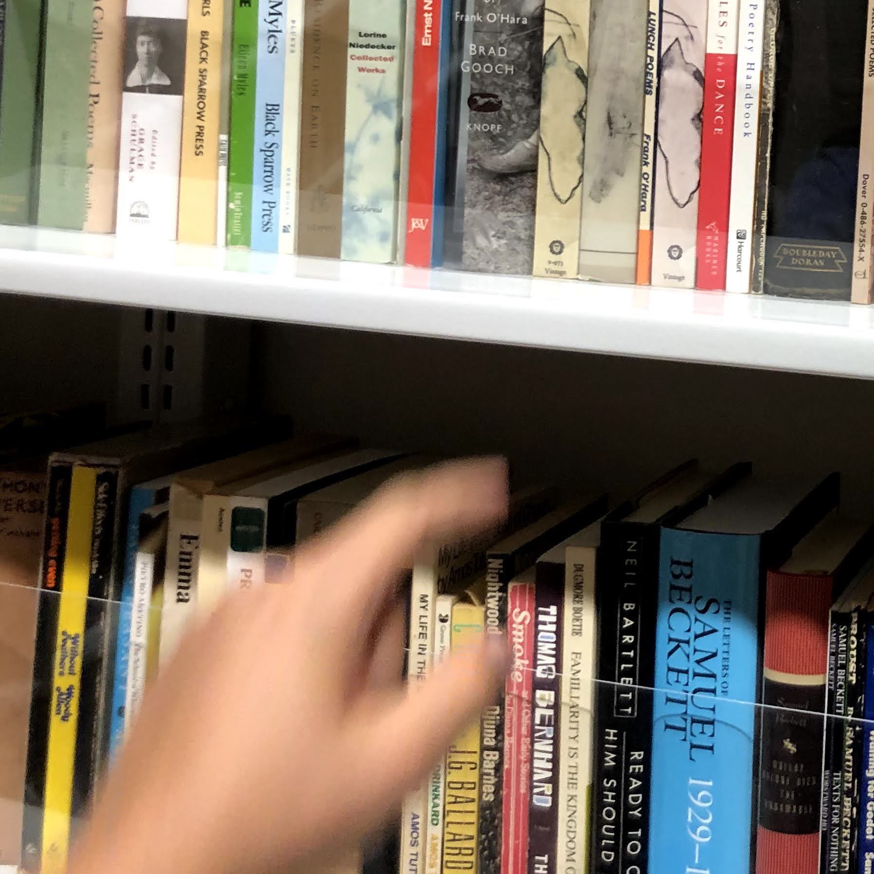 hand reaches for a book on a shelf